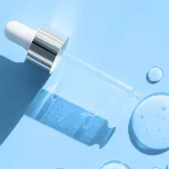 En pipett med klar vätska, som innehåller hyaluronsyra och retinol, ligger på en ljusblå bakgrund med droppar av serum.