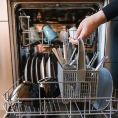 Ręka wkłada koszyk ze sztućcami do zmywarki. To oznacza, że naczynia są "dishwasher safe", czyli można je myć w zmywarce.