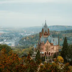 Märchenschloss im Herbstlicht, ein Juwel unter den Burgruinen NRW, thront über einer nebligen Stadt und einem Fluss.