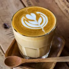 En vacker caffe latte med latte art på ett träbord. En träsked ligger bredvid.