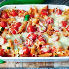 Ein köstlicher nudelauflauf vegetarisch mit Penne, Kirschtomaten und geschmolzenem Käse, garniert mit frischem Basilikum.
