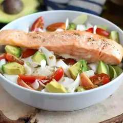 Delizioso filetto di salmone cotto su un letto di avocado, pomodorini e cipolla bianca. Un piatto leggero e gustoso, perfetto come secondi di pesce.