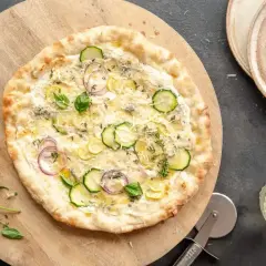 Pyszna pizza bez sosu pomidorowego z cukinią, cebulą i ziołami, podana na drewnianej desce.