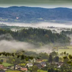 Mglisty poranek w Sudetach. Dolina spowita mgłą, zalesione wzgórza i mała wioska z domkami.