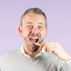 Uomo con barba che si lava i denti con uno spazzolino di legno, un gesto quotidiano per una corretta igiene dentale.