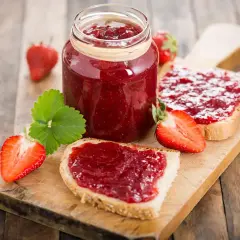 Confiture de fraises sur pain grillé, un délice qui peut faire grimper le cholestérol. Fraises fraîches et une feuille verte sur fond de bois.