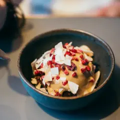 En skål med nyttig glass toppad med kokosflingor och torkade bär. En sked är på väg att ta en tugga.