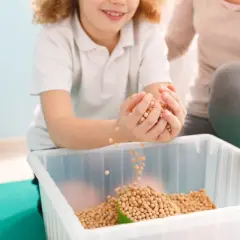 Dziecko z radością przesypuje fasolki, ćwicząc zmysły. Terapia sensoryczna pomaga w rozwoju.