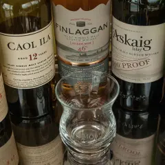 Bouteilles de whisky Islay tourbé : Caol Ila, Lagavulin, Finlaggan, Port Askaig, Ardbeg. Un verre à dégustation vide est au centre.
