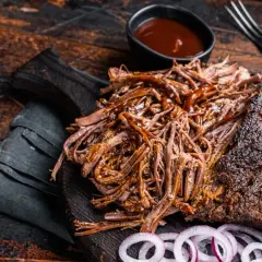 Pyszna, soczysta szarpana wołowina polana sosem BBQ, podana z krążkami cebuli na drewnianej desce.