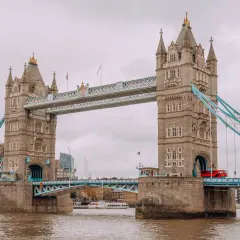 Tower Bridge w Londynie, symbol miasta, opowiada swoją historię. Czerwony autobus przejeżdża przez most, a w tle widać nowoczesne budynki.