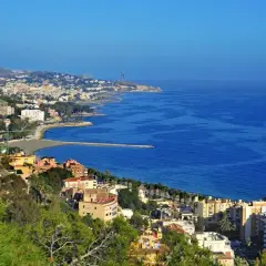 Widok na malaga plaże i miasto z zielonymi wzgórzami w tle. Błękitne morze lśni w słońcu.