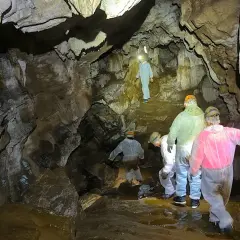 Exploradores descienden en la Cova do Rei Cintolo, iluminando formaciones rocosas y charcos de agua.