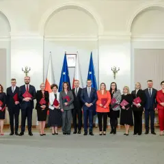 Grupa osób w eleganckich strojach, z flagami Polski w tle. Czy wśród nich jest premier Polski?