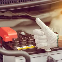 Main tenant, une main gantée fait un pouce levé près de la batterie d'une voiture qui a du mal à démarrer diesel.
