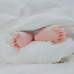 Petits pieds roses d'un bébé, emmitouflés dans une couverture blanche. Quel jour pour un baptême, une nouvelle vie commence !