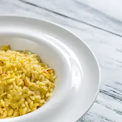 Un crémeux risotto alla milanese, orné de fils de safran, dans une assiette blanche sur fond de bois clair.