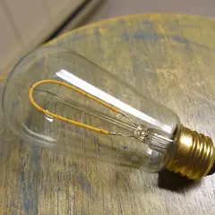 Bombilla de filamento regulable, con un diseño vintage y un filamento amarillo en forma de bucle, descansa sobre una superficie de madera desgastada.
