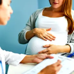 Medico spiega a donna incinta quando si fa la villocentesi, con ecografie sul tavolo.