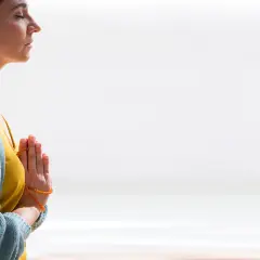 Mujer meditando con las manos juntas en posición de oración, reflejando el namasté significado yoga.
