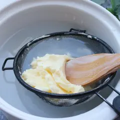 Proceso para como hacer mantequilla casera: se lava la mantequilla recién hecha en un colador con agua fría, usando una cuchara de madera.
