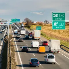 Ruch na autostradzie w Czechach, z samochodami i ciężarówkami pędzącymi z dużą prędkością. Znaki drogowe wskazują kierunki i odległości.