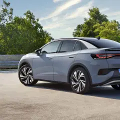 El Volkswagen ID.5 gris, con su diseño deportivo, se detiene en un día soleado, rodeado de árboles verdes y un cielo azul.