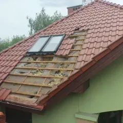 Uszkodzony dach z dachówką, widoczne okna dachowe i izolacja. Czas pomyśleć, jak uszczelnić dach przed kunami.