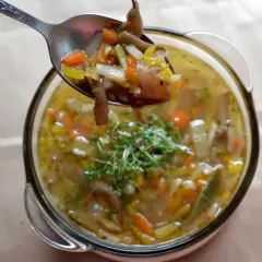 Łyżka pełna aromatycznych flaków z boczniaków, z marchewką i selerem, nad miską pełną tej pysznej zupy.