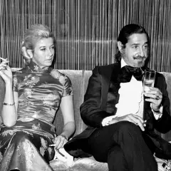 Jaime de Mora y Aragón, elegante en esmoquin, brinda con una copa mientras una mujer con vestido oriental fuma.