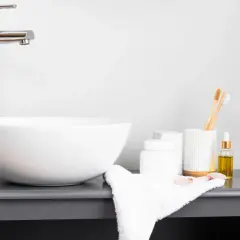 Elegancka umywalka nablatowa 50 z chromowaną baterią, obok kosmetyki i bambusowe szczoteczki do zębów.