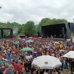 Multitud disfrutando de un concierto al aire libre en Naseiro, Viveiro. Gente bailando y animando bajo un cielo nublado.