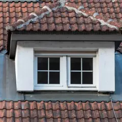 Dachgaube mit zwei Fenstern, umgeben von roten Dachziegeln. Die Bleiverkleidung zeigt, wie man eine dachgaube richtig abdichten kann.