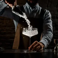 Barman aggiunge ghiaccio tritato in un calice. La corretta temperatura frigo bar bevande è fondamentale per un cocktail perfetto.