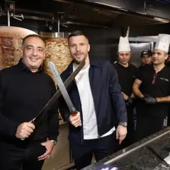 Lukas Podolski z nożami w ręku, obok niego pracownicy restauracji z kebabem.