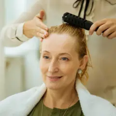Stylist czesze blondynce cienkie i rzadkie włosy, przygotowując ją do nowej fryzury.