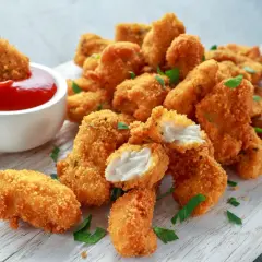 Chrupiący kurczak w panko, jeden kawałek maczany w keczupie, na desce z ziołami.