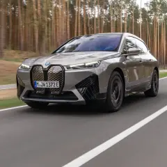 Szary BMW iX jedzie po drodze wśród drzew.