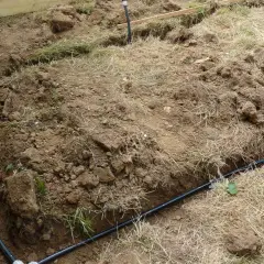 Des tranchées creusées révèlent des tuyaux noirs, prémices de réseaux enterrés pour l'irrigation ou le drainage.