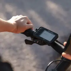 Rowerzysta trzyma kierownicę, na której zamontowany jest licznik rowerowy nie pokazuje prędkości. Obok wyświetlacz telefonu z połączeniem do Valerie.