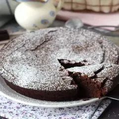 Un délicieux gâteau au chocolat saupoudré de sucre glace, parfait pour une recette gâteau au chocolat facile. Une part est coupée.