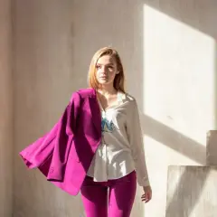 Młoda kobieta w białej koszuli i spodniach w intensywnym, **magenta kolorze**, narzucony na ramię żakiet.