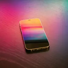 Złoty iPhone z kolorowym ekranem na drewnianym blacie. Dowiedz się, jak wgrać dzwonek na iPhone bez iTunes.