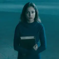 Alba Baptista, med en gammal bok i famnen, ser fundersam ut i det blåa ljuset.