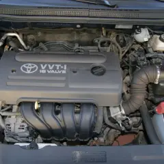 Silnik VVT-i 16 Valve z Toyoty Corolla E12. Widoczny alternator, akumulator i elementy układu dolotowego.