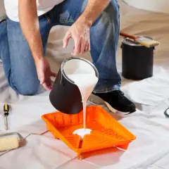 Uomo versa vernice bianca in una vaschetta arancione, pronto per pitturare soffitto con pennello. Attrezzi da pittura a portata di mano.