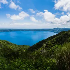 Vista panorámica de un lago azul intenso rodeado de vegetación exuberante y montañas. Un destino imperdible que ver en Nicaragua.