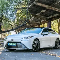 Biała Toyota Mirai, samochód przyszłości, zaparkowana pod zadaszeniem z opadłymi liśćmi wokół.