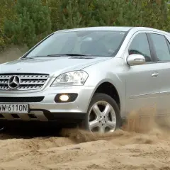 Srebrny Mercedes-Benz M-Class pokonuje piaszczysty teren, wzbijając tumany kurzu.