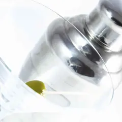 Verre à martini avec une olive, prêt pour une recette de martini gin. Shaker à cocktail en arrière-plan.